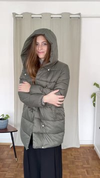 Casaco puffer verde-oliva com capuz, apresentando um design acolchoado e fechos de pressão; sobreposto a uma parte de cima cinza, com uma parte de baixo preta.