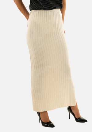 Falda maxi de punto acanalado beige con cintura alta, presenta rayas verticales y aberturas laterales. Combinada con tacones negros de punta.