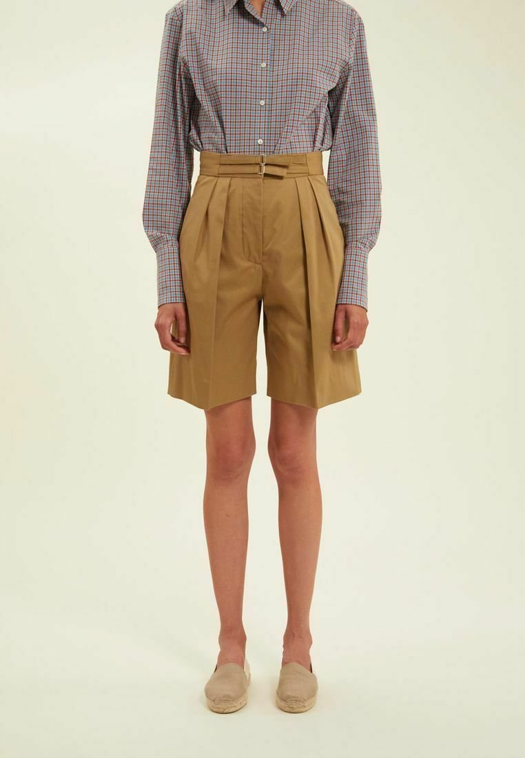 Shorts plissés beiges à taille haute avec passants de ceinture, associés à une chemise à manches longues à carreaux bleus et rouges. Texture de tissu lisse.