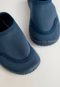 Scarpe slip-on blu navy realizzate in tessuto liscio con suola in gomma testurizzata dotata di piccoli grip rotondi e cuciture decorative lungo i bordi.