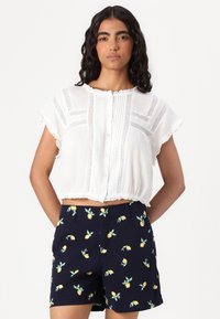Hvit kortermet bluse med blonder og korte ermer, kombinert med marineblå shorts med sitronmønster.