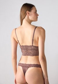 Ensemble bralette en dentelle et string de couleur brun foncé, avec des motifs floraux, des bretelles fines et une texture douce.