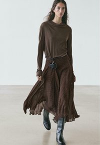 Brown long-sleeve top with a relaxed neckline, paired with a brown polka-dot skirt. Accessories include a small black bag and black knee-high boots.