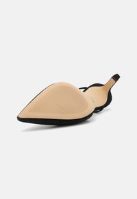 Black suede pointed-toe shoe with a smooth beige sole, featuring a low back design and a textured grip pattern on the sole.