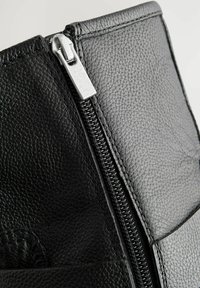Black textured leather boot with a visible silver zipper detail along the side. Features angular design elements and smooth stitching.