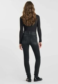 Jean skinny noir taille haute avec une texture lisse, dotés de poches arrière et d'une fermeture à glissière, associés à un haut noir à manches longues.