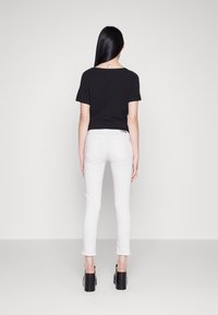 Top negro de manga corta, jeans ajustados blancos y tacones de plataforma negros. El top tiene un escote redondeado y está hecho de una tela suave.