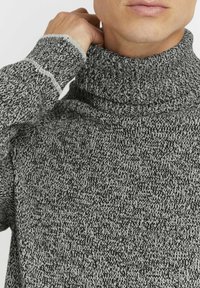 Siv šivani pulover s turtleneck ovratnikom in teksturiranim dizajnom. Ima tesno prilegajoč ovratnik in kontrastni šiv v bližini rokava.