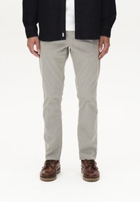Hellgraue, strukturierte Hosen im Slim Fit, kombiniert mit einem dunklen Button-Down-Hemd. Braune Schnürschuhe mit dickem Absatz sorgen für einen Kontrast.