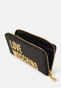 Carteira preta com fecho em zíper com a inscrição em dourado "LOVE MOSCHINO" e puxador de zíper em dourado com detalhe de coração, parcialmente aberta mostrando os slots para cartões.