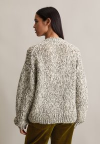 Suéter de punto grueso en tonos gris y crema, con cuello redondo y mangas oversized, hecho de un hilo texturizado y un corte relajado.