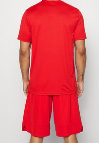 Camiseta atlética roja y pantalones cortos, hechos de una tela suave. La camiseta tiene un escote redondo y mangas cortas; los pantalones cortos presentan un ajuste relajado y detalles texturizados.