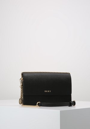 Czarna skórzana torebka typu crossbody DKNY z złotym łańcuszkiem i logo, prezentowana na białym piedestale na jednolitym tle.