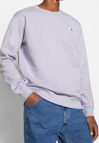 Felpa lavanda con scollatura a girocollo, polsini a costine e un dettaglio ricamato; abbinata a jeans in denim blu che mettono in risalto una vestibilità comoda.