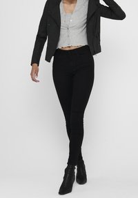 Veste de motard en cuir noir, top court gris et jean skinny noir. Texture lisse avec un design ajusté et des bottes noires montantes.