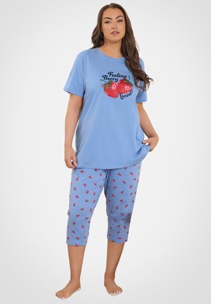 Mujer de pie descalza con pijama azul con estampado de fresas y texto "Feeling Berry Good!" en la camiseta.