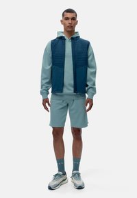 Šviesiai mėlynas gobtuvėlis, tamsiai mėlynas be rankovių liemenė su siuvinėtu raštu, atitinkantys šortai ir sportiniai bateliai su tekstūruota pada.