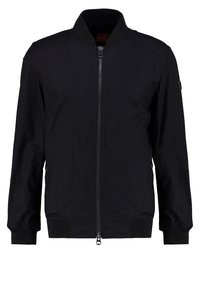 Veste bomber noire avec fermeture éclair à l'avant, poignets et taille côtelés, avec un petit écusson sur la manche gauche.