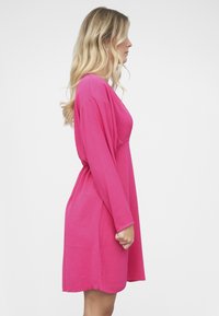 Vaaleanpunainen mekko, joka on valmistettu kevyestä kankaasta. Mekossa on väljä istuvuus, pitkät hihat ja pyöreä helma. Sivukuva korostaa sen virtaavaa siluettia.