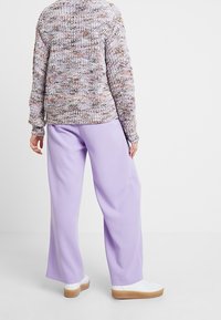 Pull en tricot avec un motif moucheté en gris et beige, associé à un pantalon large lilas. Baskets blanches avec une semelle texturée.
