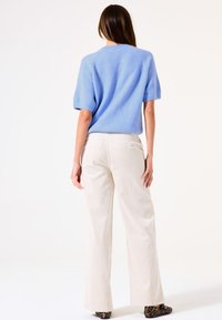 Helleblaue, kurzärmelige Strickjacke kombiniert mit hoch taillierten, off-white weit geschnittenen Hosen und Schuhen mit Leopardenmuster. Glatte Texturen sind sichtbar.