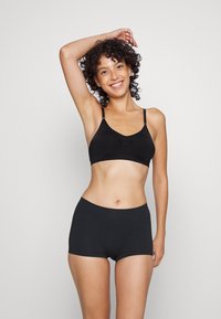 Black cotton bralette with adjustable straps and a gathered detail at the center, paired with matching black cotton shorts.
