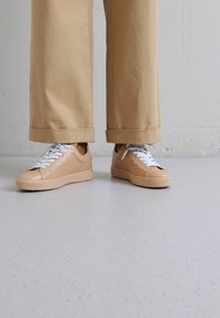 Zapatillas de cuero beige con cordones blancos, que presentan un diseño cosido a lo largo de los laterales y una suela de goma texturizada.