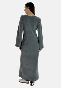 Vestido gris de manga larga, hecho de una tela suave, con un escote redondo y un corte holgado, que presenta una silueta recta y sin patrones visibles.