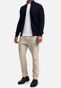 Marineblauer Reißverschluss-Pullover mit strukturiertem Strickmuster, kombiniert mit einem weißen T-Shirt und beigen Hosen, abgerundet mit schwarzen Schnürstiefeln.