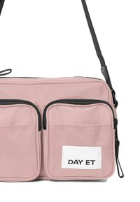 Borsa a tracolla rosa con due tasche frontali con zip e un'etichetta bianca con la scritta "DAY ET". Presenta una tracolla nera regolabile.