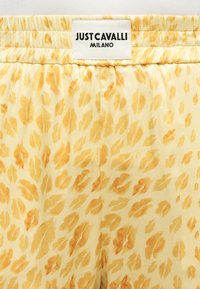 Tissu jaune et beige à motifs avec une taille élastique et une étiquette blanche "Just Cavalli Milano" cousue au centre.