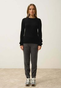 Czarny sweter z prążkowanego materiału w zestawieniu z szarymi spodniami dresowymi i butami sportowymi. Sweter ma długie rękawy i okrągły dekolt.