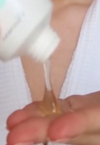 Klar vätska som hälls från en vit flaska in i en hand. Texturen är viskös, med en lätt bärnstenston. Bakgrunden är suddig.