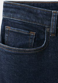 Jean en denim bleu foncé en gros plan montrant la poche avant, la petite poche à monnaie, la passante de ceinture et les détails de couture orange.