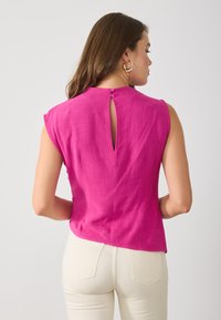 Fuchsia ärmlös topp med rund halsringning, med en nyckelhålsdetalj på baksidan som säkras med två knappar; tillverkad av ett strukturerat tyg.