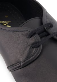 Close-up van een zwart leren schoen met een gestructureerd oppervlak en een zwart veter op het bovenste gedeelte.