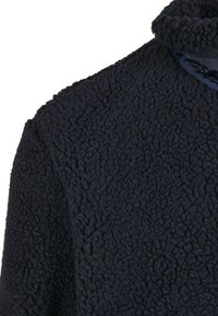 Tumesinine fliisjope tekstuurse pinnaga ja kõrge kraega. Kangas on pehme, sametine ja väikese, ebaregulaarselt mustriga.