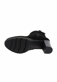 Botte de cheville en daim noir avec un talon épais, semelle en caoutchouc texturé avec de profondes rainures, et détail de sangle à boucle sur le côté.
