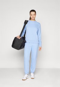 Sweatshirt bleu clair et pantalon assorti en matériau doux, associés à des baskets blanches et un sac de sport noir. Texture lisse, design décontracté.