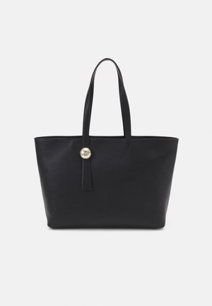 Czarna skórzana torba typu tote z długimi uchwytami i pojedynczym złotym guzikiem na jednym pasku, na jasnym, jednolitym tle.