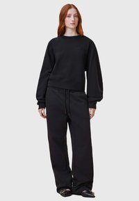 Sudadera negra y pantalones de chándal a juego hechos de tela suave. La sudadera cuenta con un dobladillo y puños acanalados, con un sutil detalle de logo en el pecho.