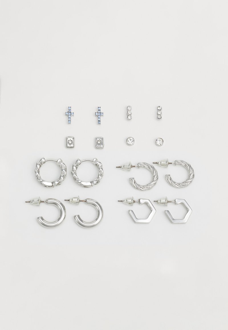 Set of silver earrings including cross studs, hooped designs, and hexagonal accents, featuring various textures and embellishments.
