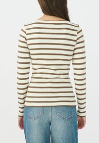 Maglietta a maniche lunghe a righe con strisce orizzontali crema e marroni, caratterizzata da un collo rotondo e una vestibilità aderente, abbinata a jeans azzurri chiari.