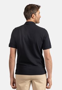 Černé polo tričko vyrobené z bavlny, má klasický límec a krátké rukávy, hladkou strukturu a přiléhavý střih.