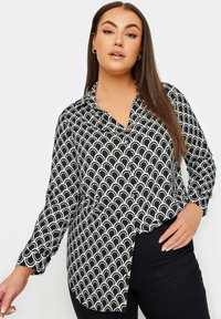 Czarna i biała koszula z długim rękawem, wzorzysta w fale, z zaokrąglonym dołem. Gładka tkanina, luźny krój.