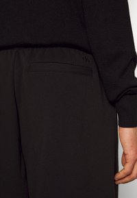 Svart stickad tröja i kombination med svarta byxor med bakficka. Subtil "CK"-logotyp präglad på fickan. Slät textur och tapered design.