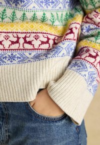 Strickpullover mit geripptem Halsausschnitt und Bündchen, der bunte nordische Muster zeigt, hauptsächlich in Rot, Blau, Gelb und Grün auf einem crèmefarbenen Hintergrund.