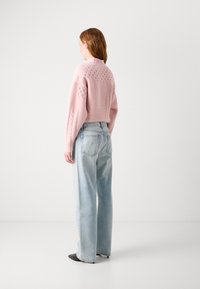 Pink knitted sweater with textured patterns paired with light wash, loose-fitting jeans. Black pointed-toe heels are worn.