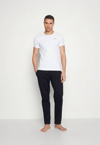 Fehér, kerek nyakú rövid ujjú póló, fekete, karcsúsított nadrággal párosítva. A ruházat puha anyagból készült, minimális díszítéssel.