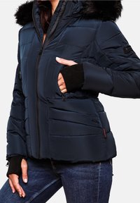 Granatowa kurtka puchowa z kapturem z sztucznego futra, zapinana na zamek błyskawiczny, z ściągaczami przy mankietach i kieszeniami. Posiada pikowaną fakturę i dopasowany krój.